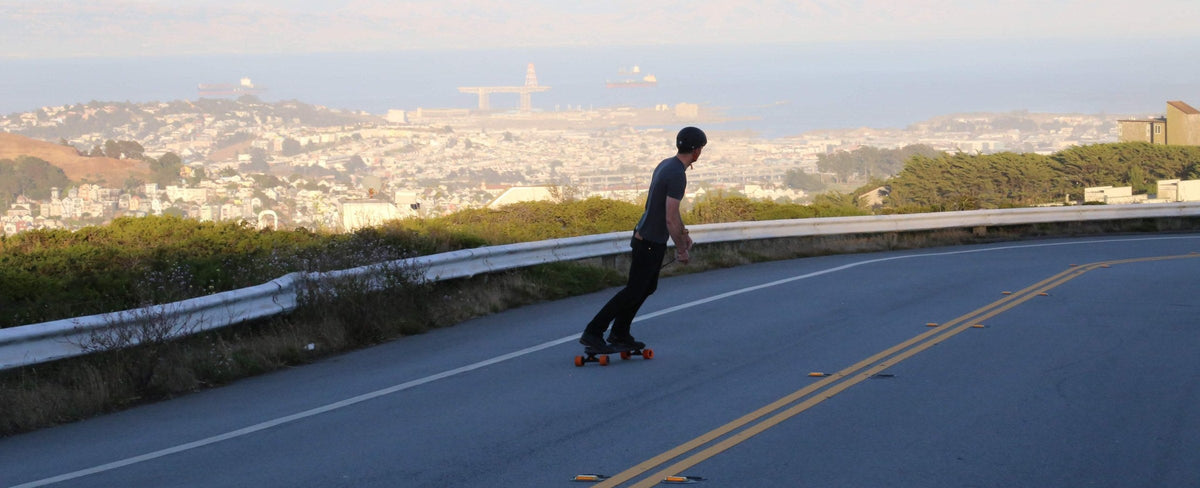 Rider on an electric skateboard coasting down a hillside road above San Francisco